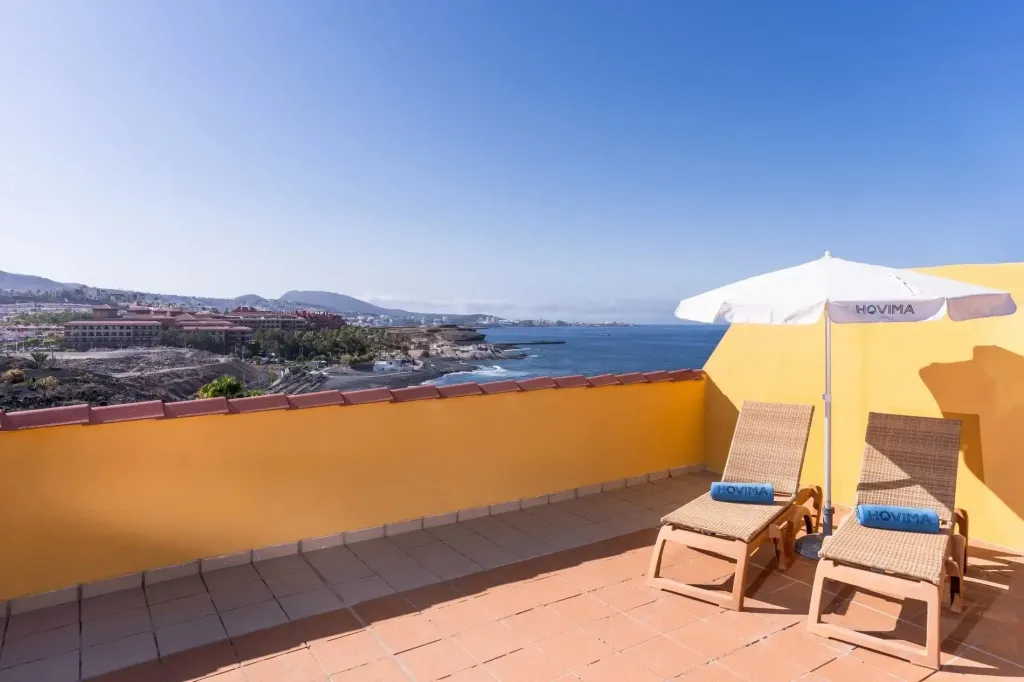 Terrasse avec transats et vue sur la mer et les montagnes.