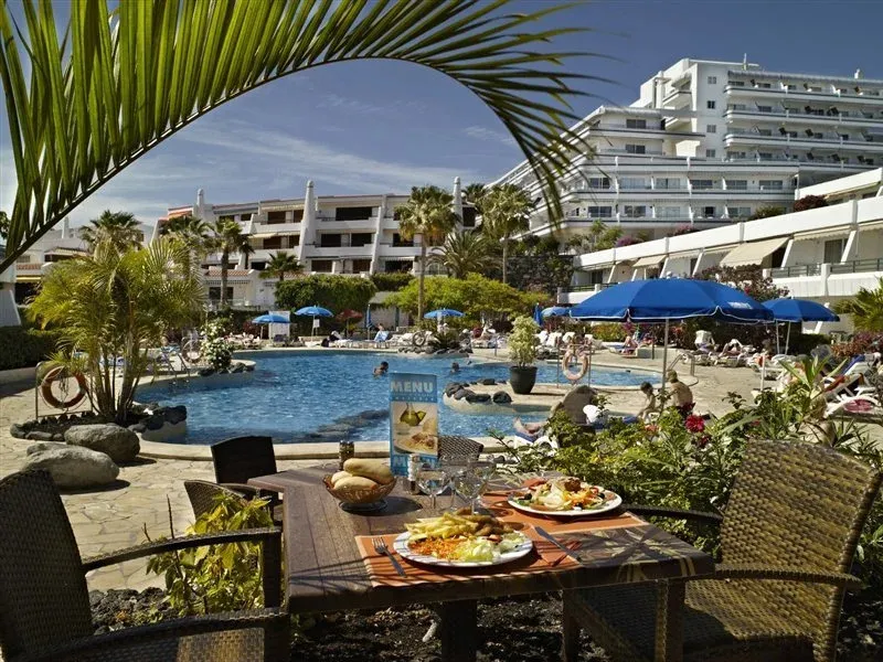 Une table est dressée avec des plats et des boissons au bord d'une piscine ensoleillée.