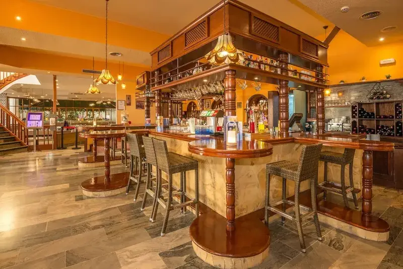 Un comptoir de bar en bois massif avec des tabourets hauts et des bouteilles exposées.