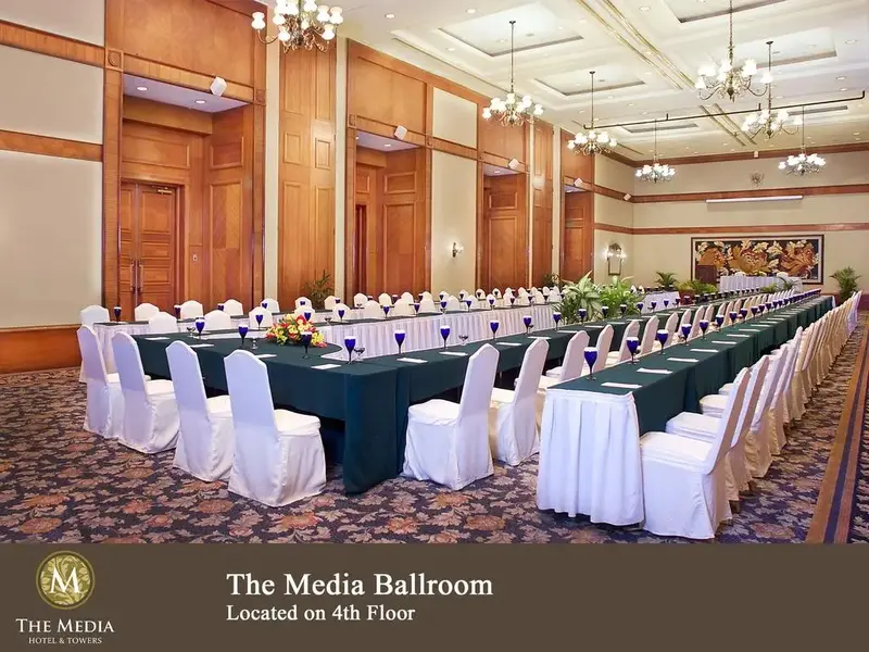 Une longue table de réunion est dressée dans une salle aux boiseries claires et aux lustres.