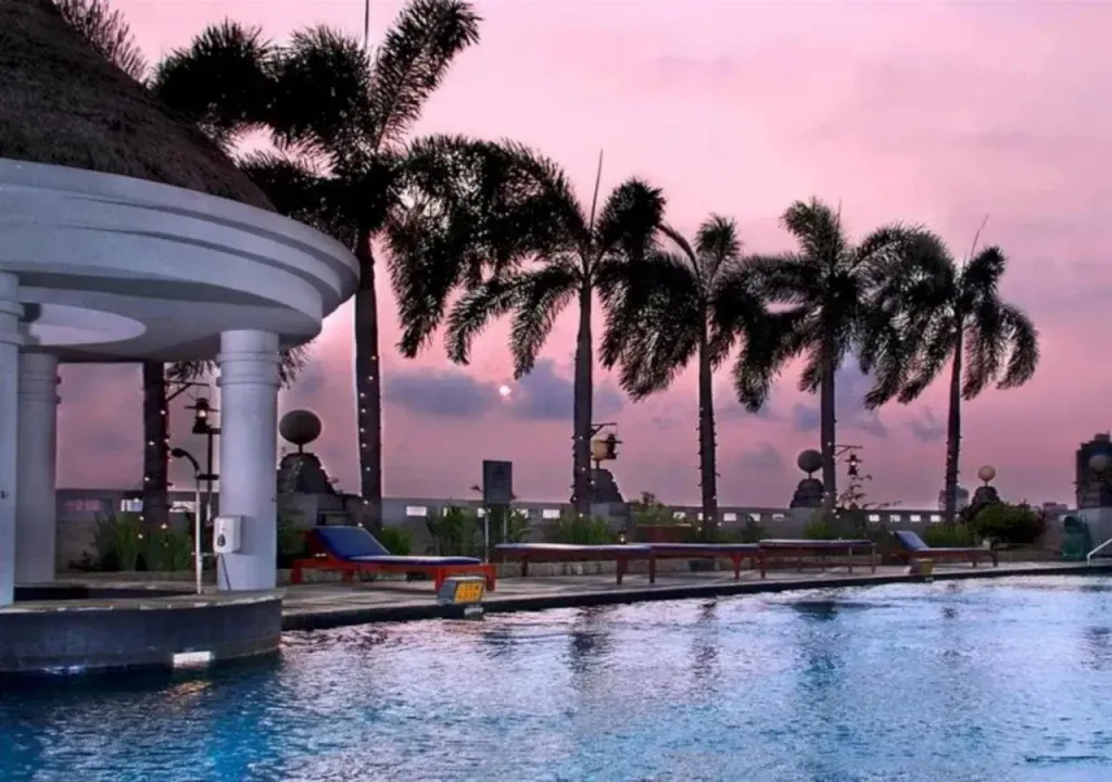 Une piscine bordée de transats et de palmiers au coucher du soleil.