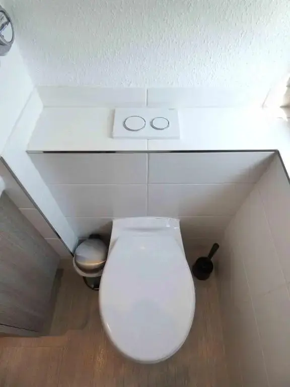 Toilettes avec carrelage mural et chasse d'eau intégrée.