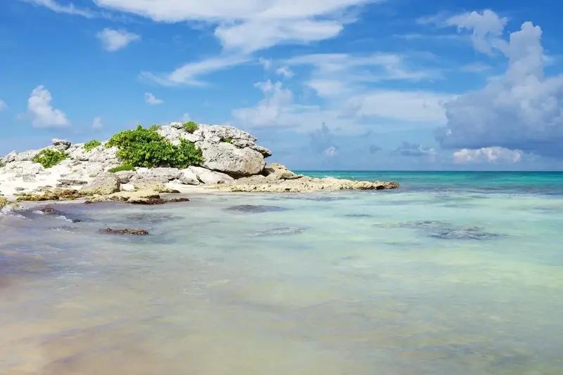 Une plage de sable blanc borde une eau turquoise sous un ciel nuageux.
