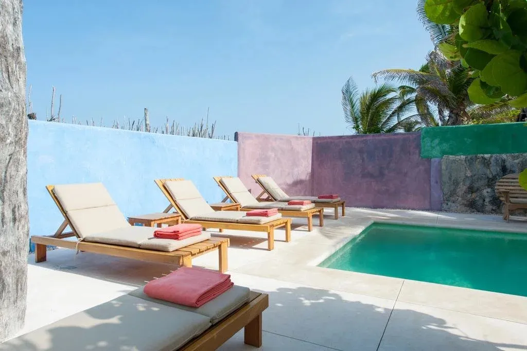 Transats alignés au bord d'une piscine turquoise dans un espace extérieur coloré.