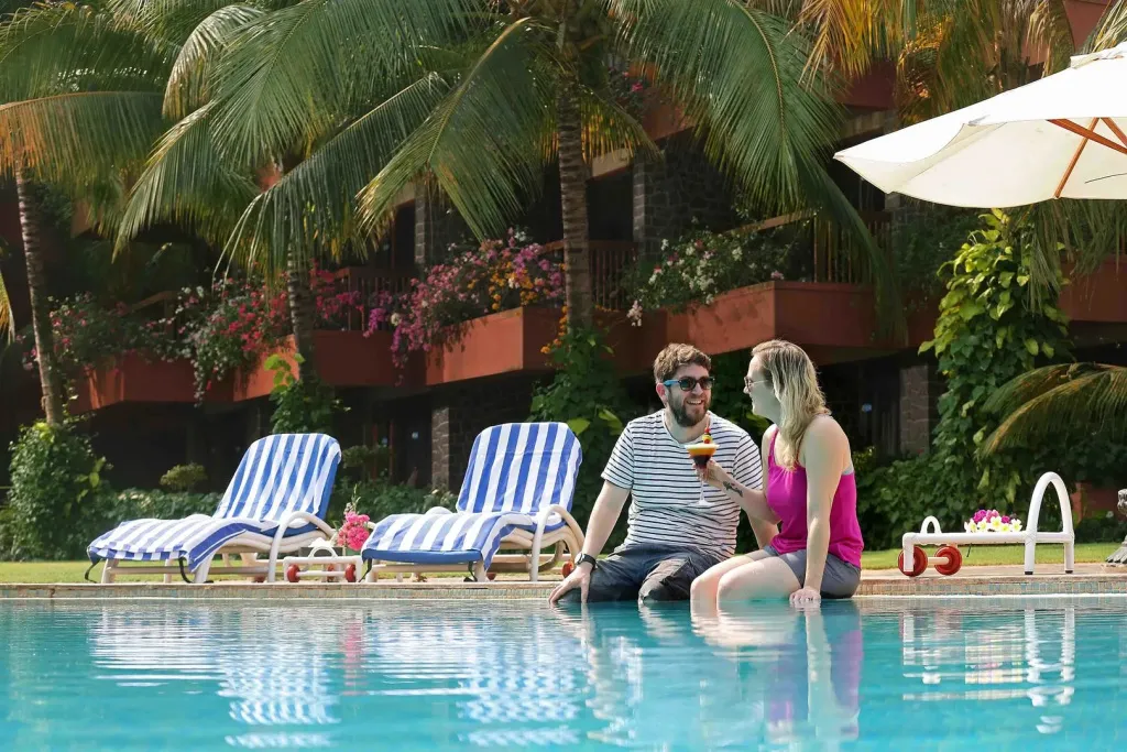 Un couple se détend au bord d'une piscine ensoleillée, avec des transats et une végétation luxuriante en arrière-plan.