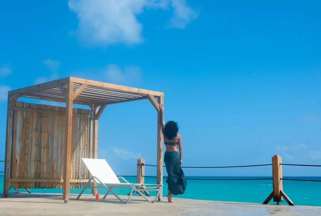 Une personne se tient près d'un espace de détente en bois avec vue sur la mer.