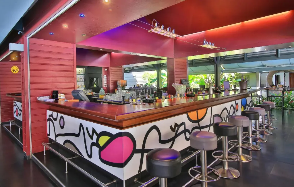 Un long comptoir de bar coloré avec des tabourets, éclairé par des néons.