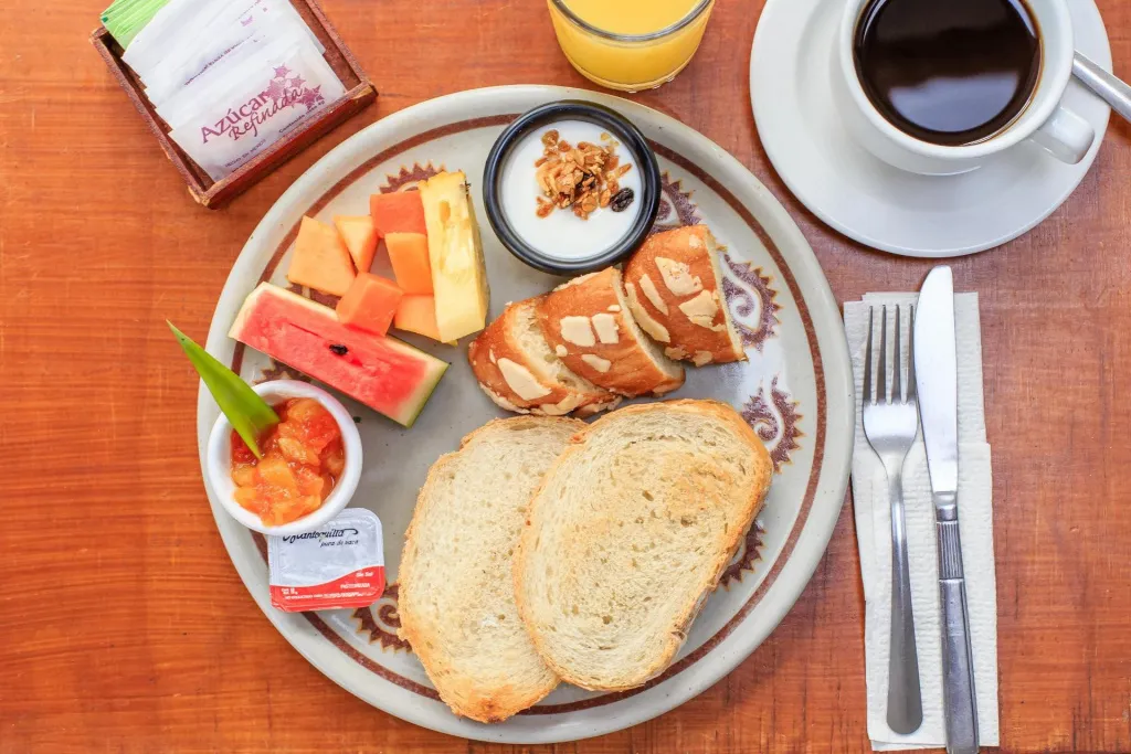 Un petit-déjeuner avec des fruits frais, du pain et une boisson chaude est présenté sur une table en bois.
