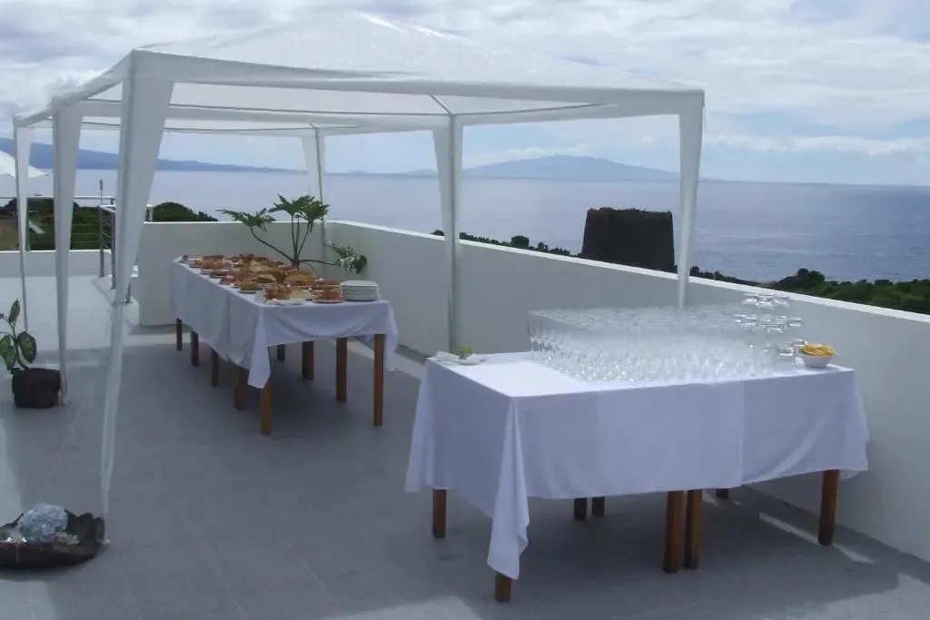 Tables dressées avec des plats et des boissons sur une terrasse ensoleillée avec vue sur la mer.