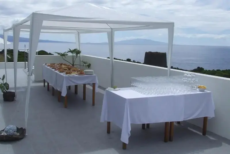 Tables dressées avec des plats et des boissons sur une terrasse ensoleillée avec vue sur la mer.