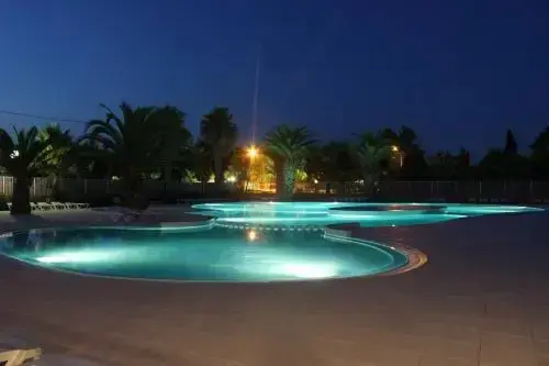 Piscine illuminée au crépuscule avec végétation tropicale.