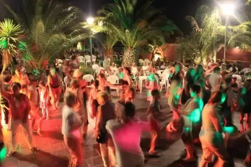 Une foule de personnes se divertit en extérieur sous des palmiers illuminés.