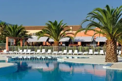 Une piscine bordée de transats et de palmiers devant un bâtiment aux couleurs vives.