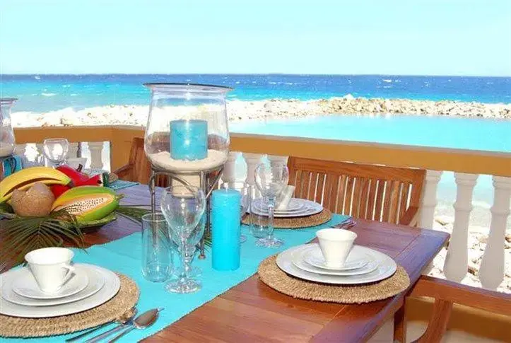 Une table dressée avec des fruits et de la vaisselle offre une vue sur la mer turquoise.