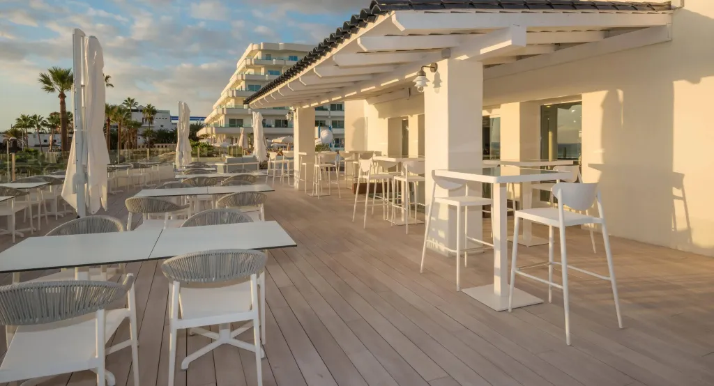 Terrasse aménagée avec tables basses et chaises blanches, sous une structure ajourée.