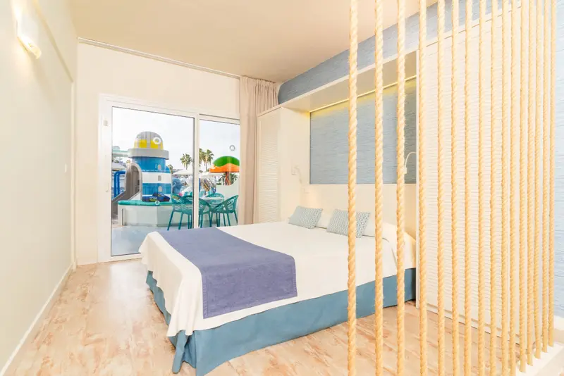 Une chambre lumineuse avec un lit double et une vue sur une piscine pour enfants.
