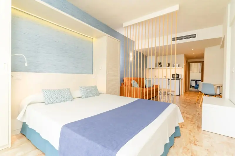 Une chambre lumineuse avec un grand lit et un espace salon attenant.