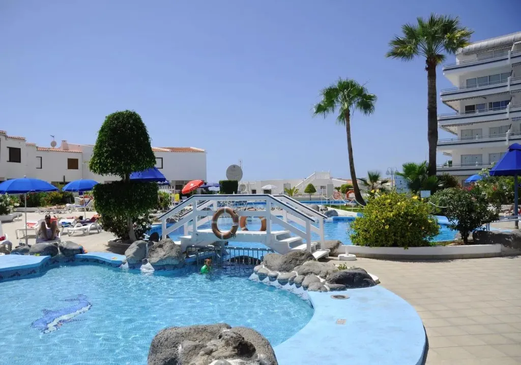 Piscine avec ponton et palmiers sous un ciel bleu.