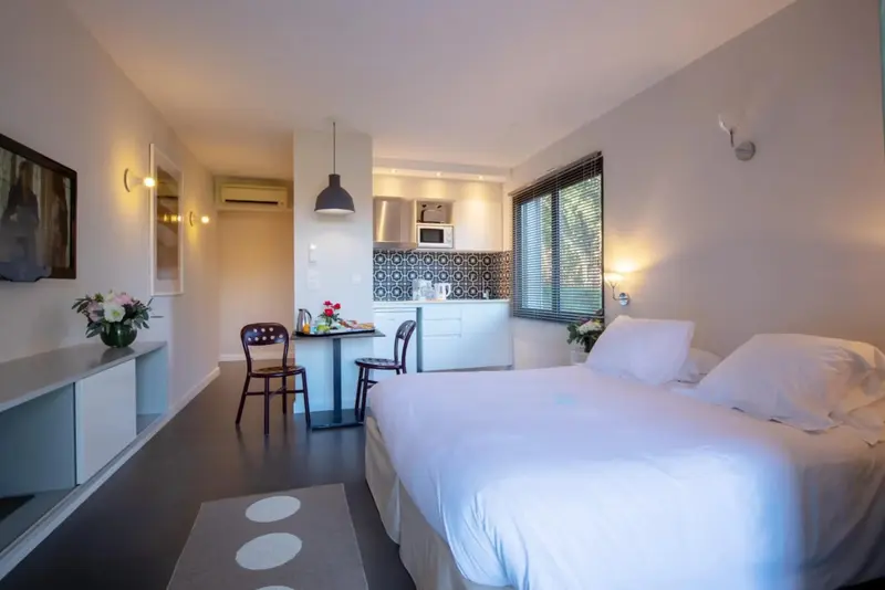 Une chambre lumineuse avec un lit blanc et une petite cuisine.