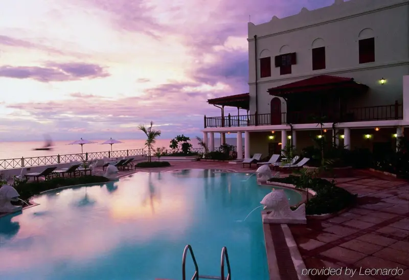 Une piscine turquoise reflète les couleurs d'un ciel crépusculaire devant un bâtiment blanc.
