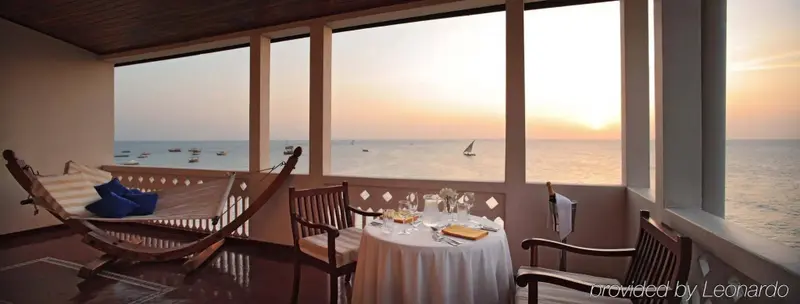 Une table est dressée devant de larges baies vitrées donnant sur la mer au coucher du soleil.