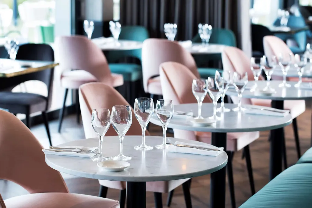 Tables rondes dressées avec couverts et verres dans une salle lumineuse.