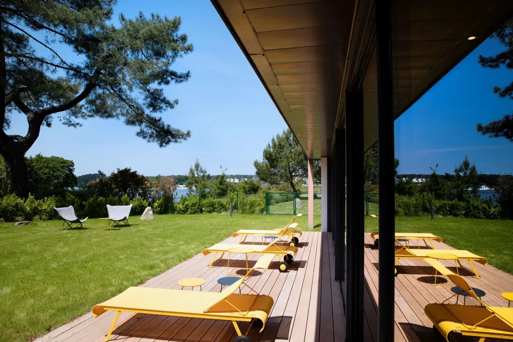 Terrasse en bois avec transats jaunes donnant sur une pelouse et la mer.