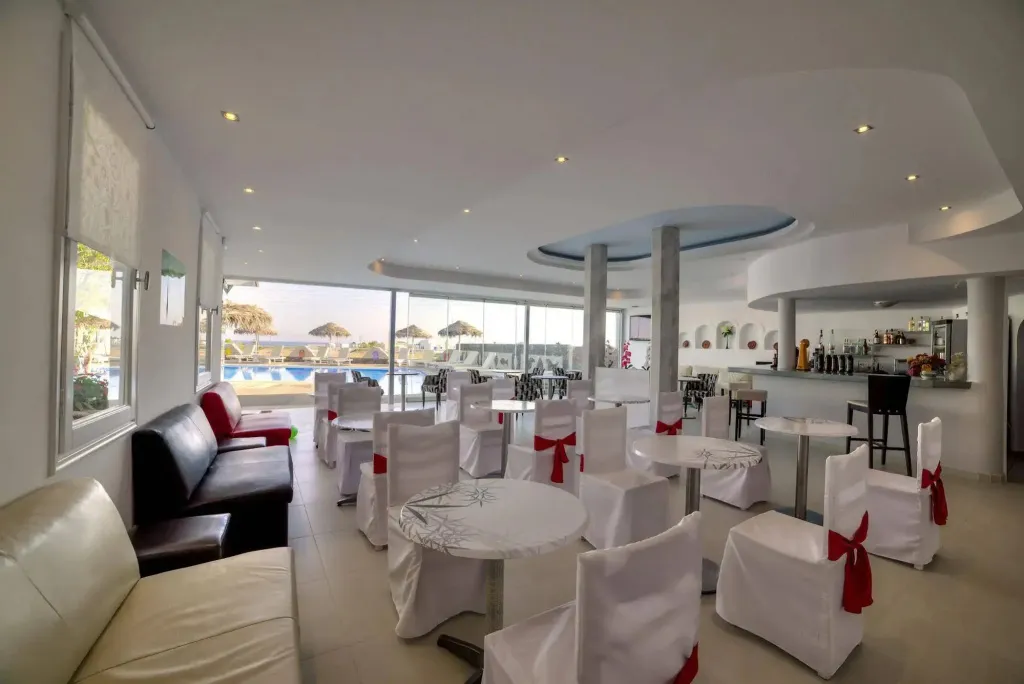 Espace lumineux avec tables et canapés près d'une grande baie vitrée donnant sur une piscine.