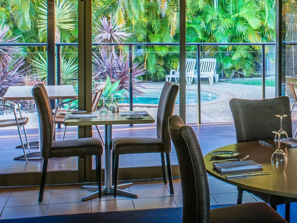 Tables dressées dans une salle à manger lumineuse donnant sur une piscine et une végétation tropicale.