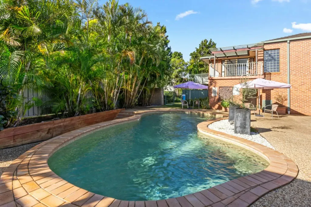 Une piscine rectangulaire bordée de briques et entourée de végétation luxuriante.