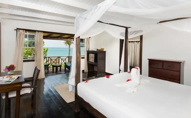 Une chambre lumineuse avec un lit à baldaquin donnant sur une terrasse et la mer.