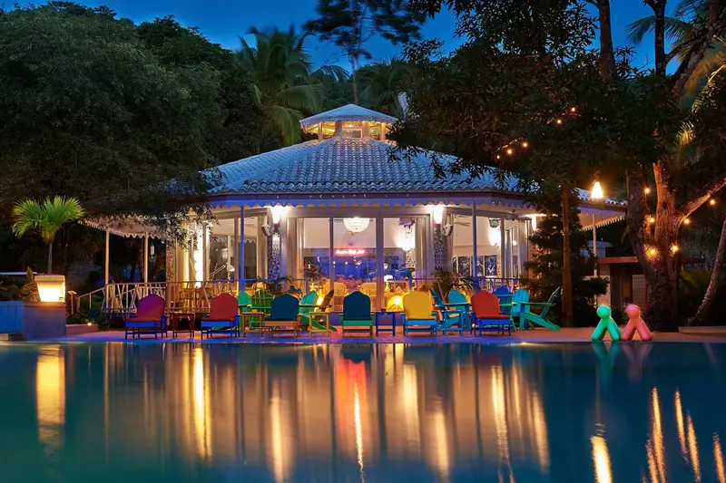 Une salle lumineuse s'ouvre sur une piscine reflétant les lumières colorées.