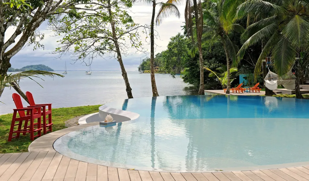 Piscine bleue à débordement avec chaises longues rouges et végétation tropicale.