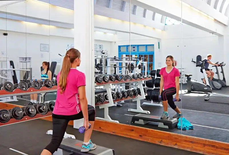 Une femme fait de l'exercice avec des haltères dans une salle de sport lumineuse.