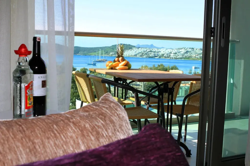 Une table avec des fruits et des boissons est mise en valeur sur une terrasse ensoleillée avec vue sur la mer.