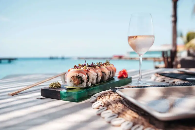 Assiette de sushis et verre de vin sur une table en bois face à la mer.