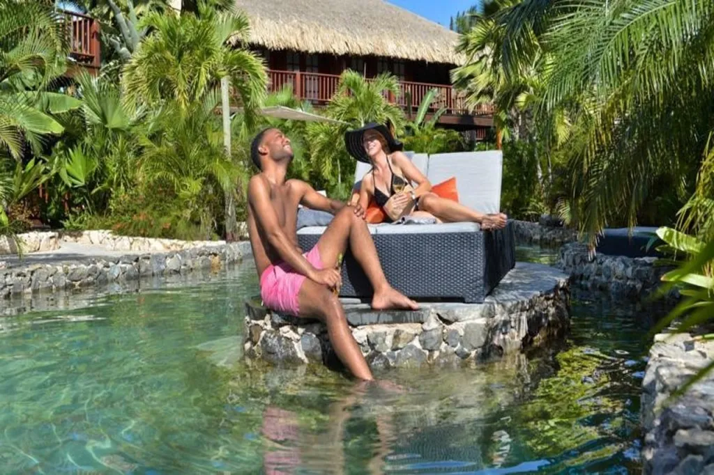 Un couple se détend au bord d'une piscine naturelle entourée de végétation tropicale.