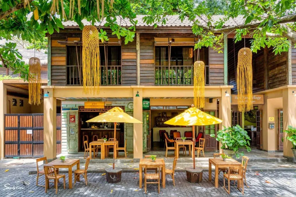 Terrasse ombragée avec tables et chaises devant un bâtiment à deux étages.