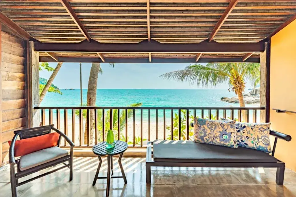 Terrasse ombragée donnant sur une plage de sable fin et une mer turquoise.