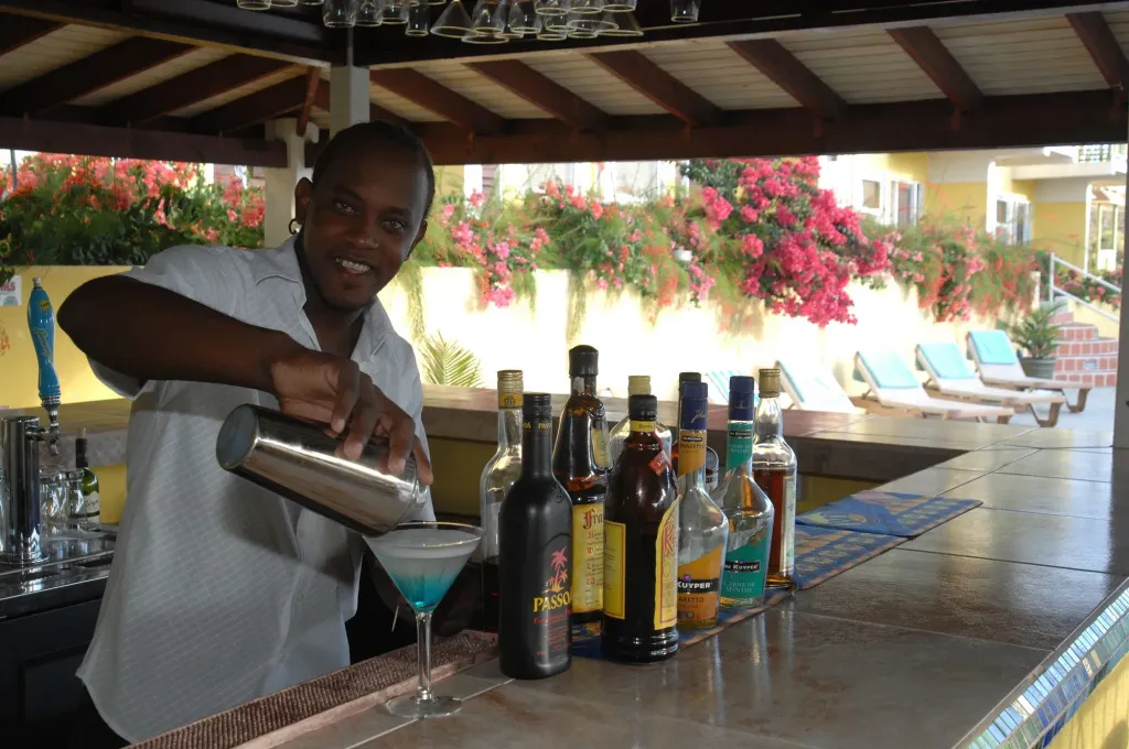 Un barman prépare un cocktail bleu derrière un comptoir bien garni.