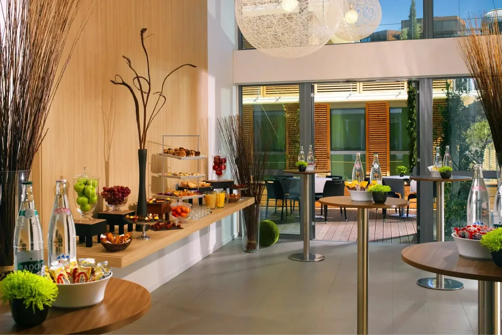 Un buffet propose des fruits, des pâtisseries et des boissons dans un espace lumineux et moderne.