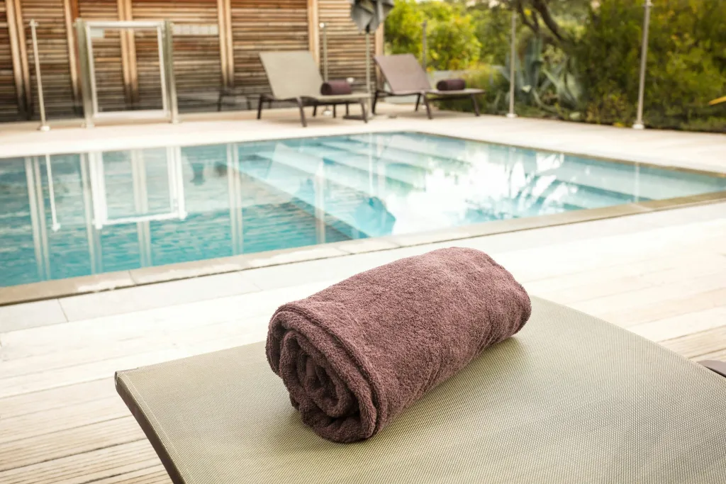 Serviette roulée sur un transat au bord d'une piscine rectangulaire.