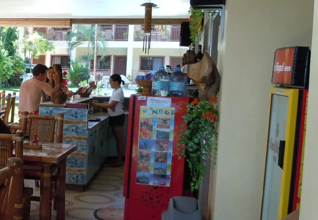 Un bar extérieur avec des clients et une employée près d'une piscine.