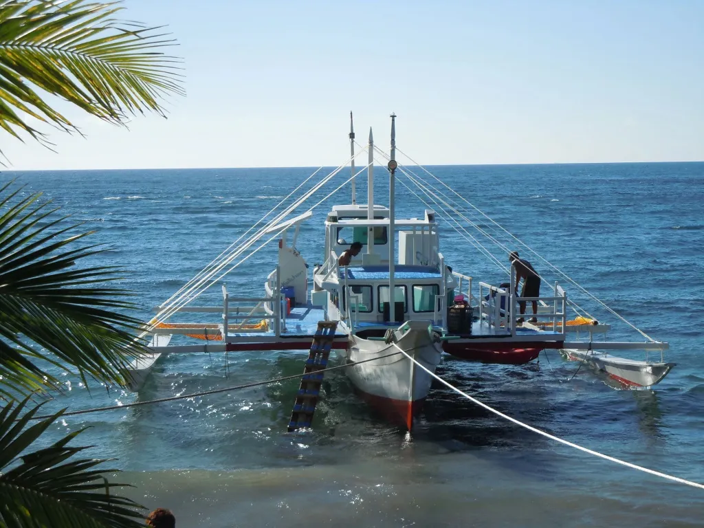 Un bateau blanc amarré dans une eau turquoise, avec des personnes à bord.