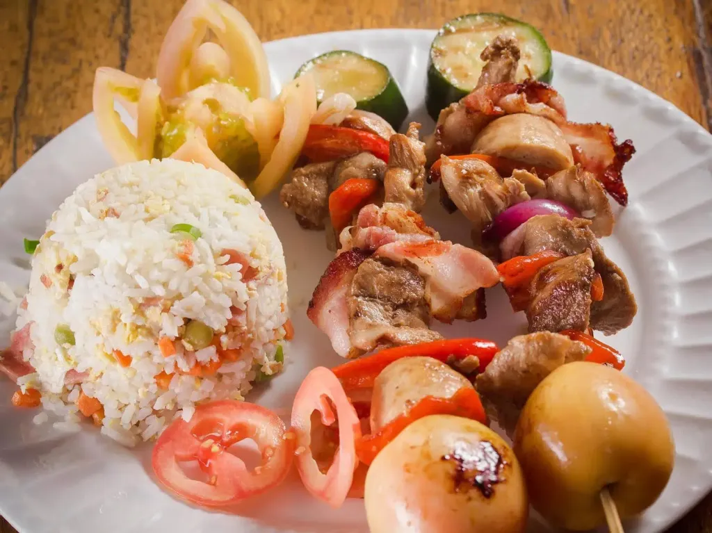 Assiette garnie de riz, de brochettes de viande et de légumes.