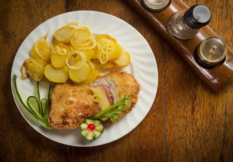 Assiette de viande panée accompagnée de pommes de terre et d'une garniture.