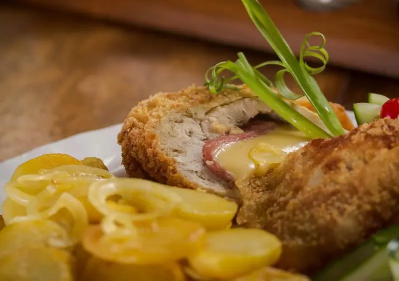 Assiette de viande panée farcie au fromage et jambon, accompagnée de pommes de terre et de légumes.