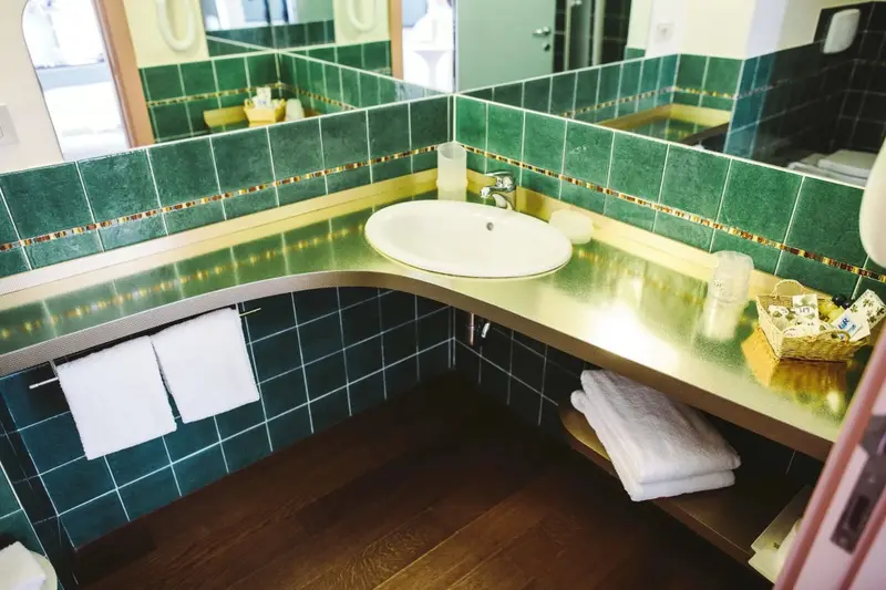 Une salle de bain lumineuse avec des carreaux verts et un lavabo blanc.