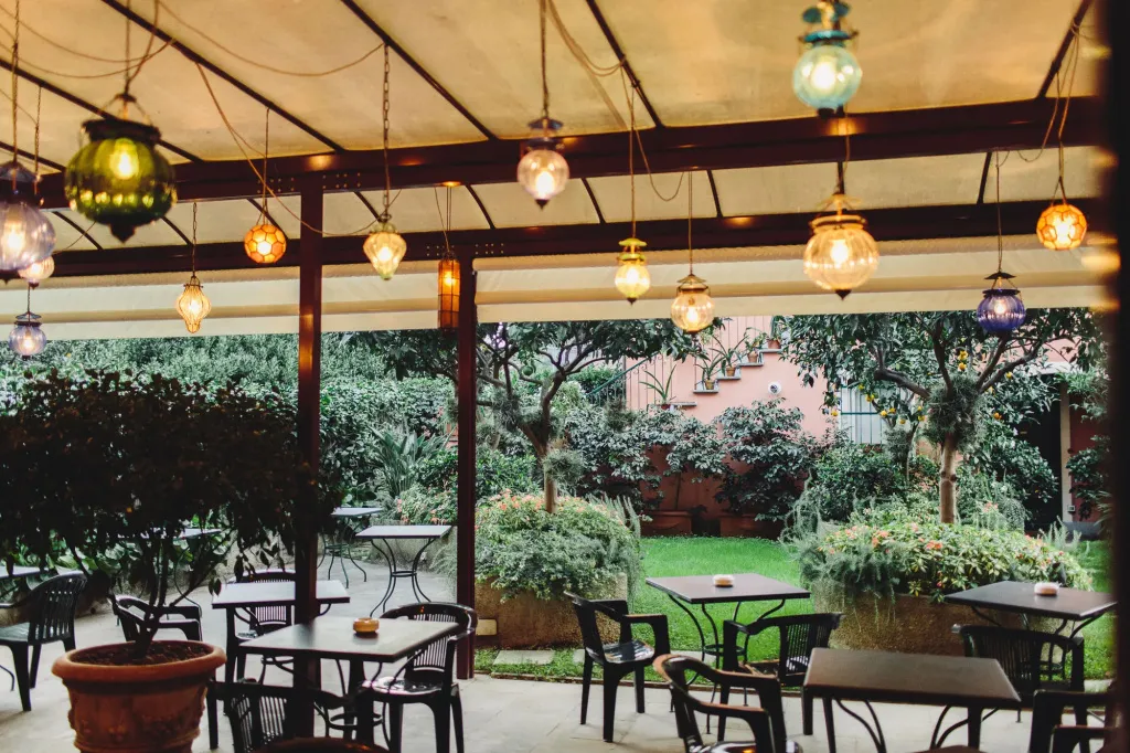 Terrasse ombragée avec tables et lanternes colorées donnant sur un jardin.