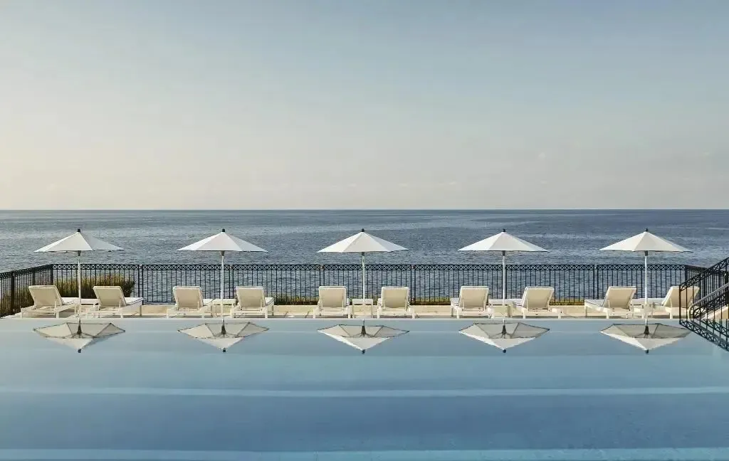 Transats blancs alignés au bord d'une piscine à débordement face à la mer.